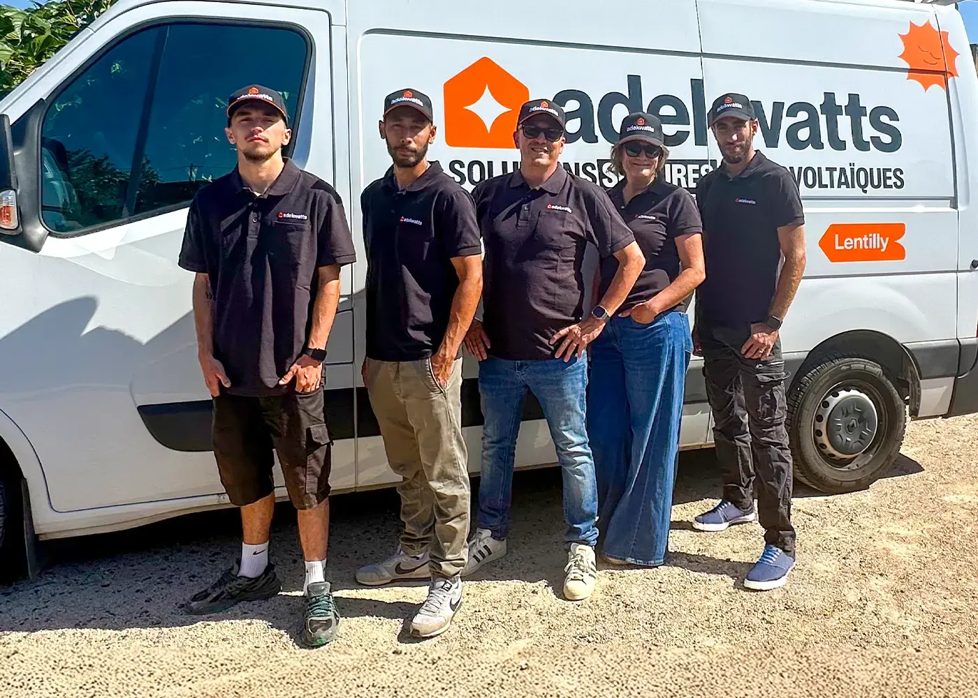 Photo de groupe de l’équipe adekwatts Rhône à Lentilly, en polos noirs et casquettes, devant un véhicule adekwatts.