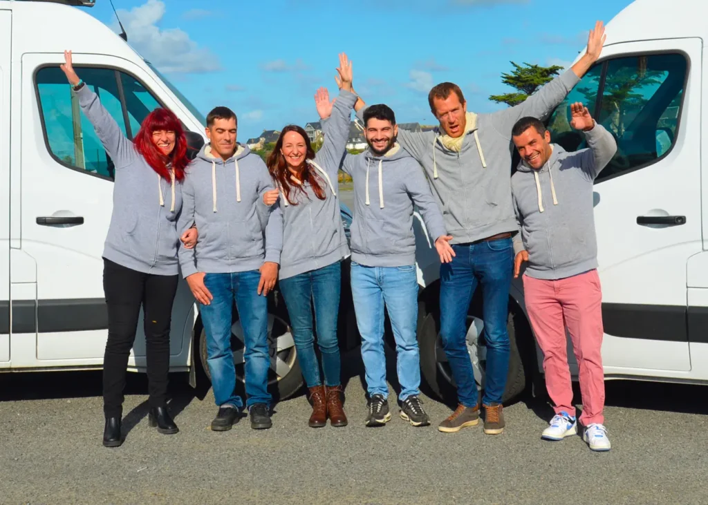 Équipe adekwatts Loire-Atlantique souriante, en sweat gris, posant bras levés devant deux fourgons blancs.
