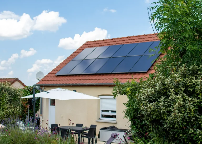 Panneaux solaires noirs sur toiture en tuiles rouges au-dessus d’une terrasse de jardin.
