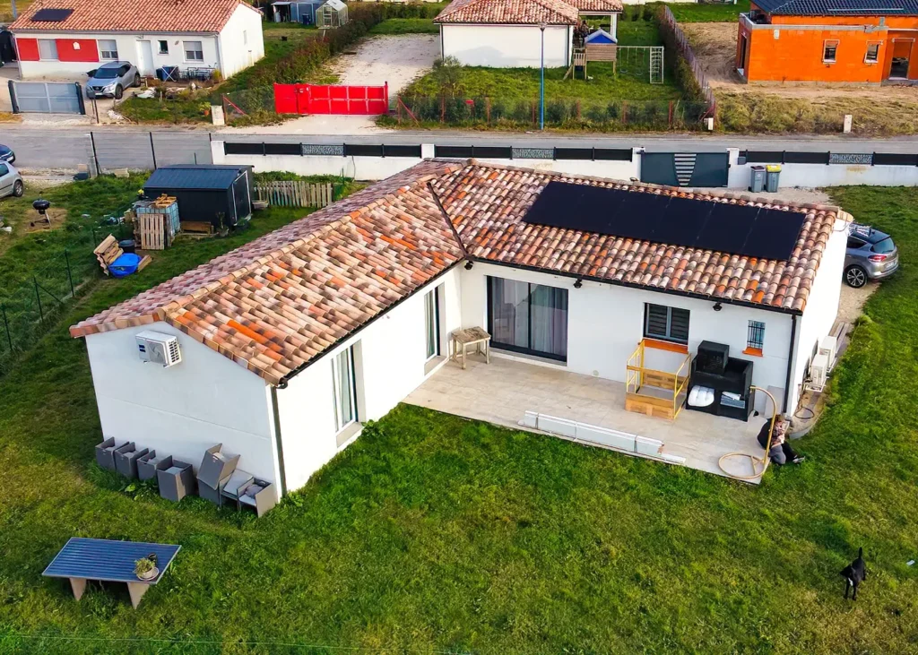 Vue aérienne d’une maison de plain-pied avec toiture en tuiles équipée de panneaux photovoltaïques noirs, terrasse et jardin.