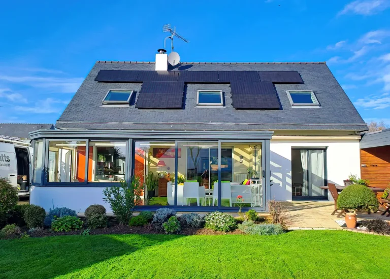Maison avec véranda et jardin, équipée de panneaux photovoltaïques noirs sur la toiture en ardoise.