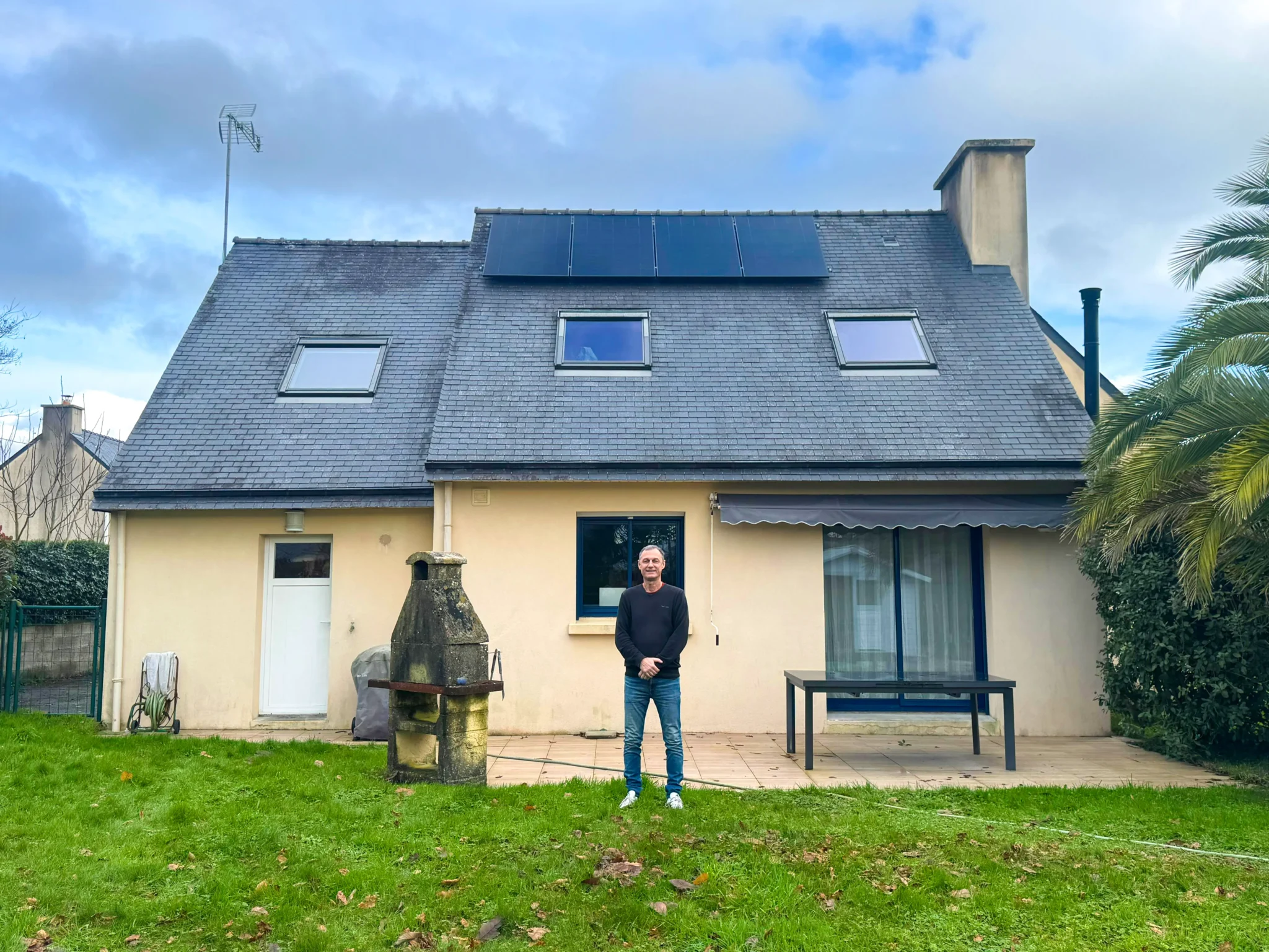 Maison à Mellac (29300) avec une installation photovoltaïque de 2 kWc sur toiture en ardoise, propriétaire debout dans le jardin.