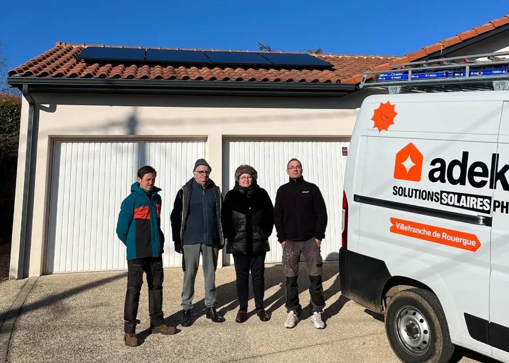 Équipe Adekwatts devant une maison équipée de panneaux solaires, avec le camion “Villefranche-de-Rouergue” au premier plan.