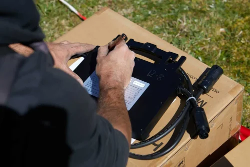 Technicien préparant un équipement électrique photovoltaïque avec câbles et connecteurs, posé sur un carton, en extérieur.